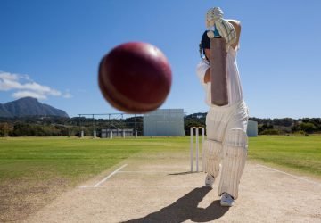Full length of batsman playing cricket on pitch against blue sky during sunny day