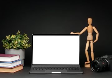 Open laptop with wooden mannequin on table against black background copy space